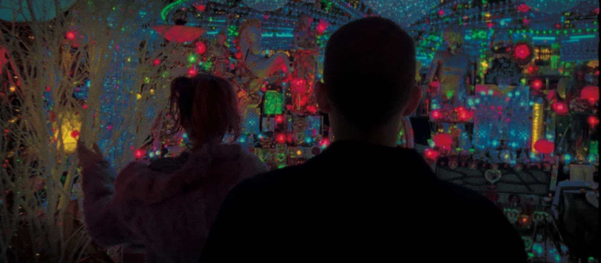 A man and a woman standing in front of several colorful lights in a cornershop